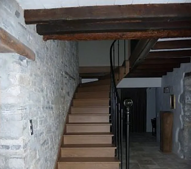 Escalier en bois sous plafond à poutres, mur en pierre
